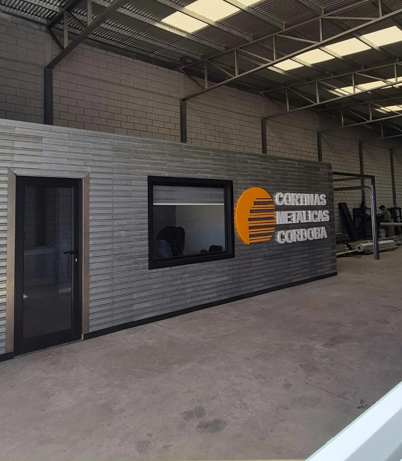 Oficina de CMC Cortinas Metálicas dentro del taller, revestida con tablillas galvanizadas y con el logo de la empresa